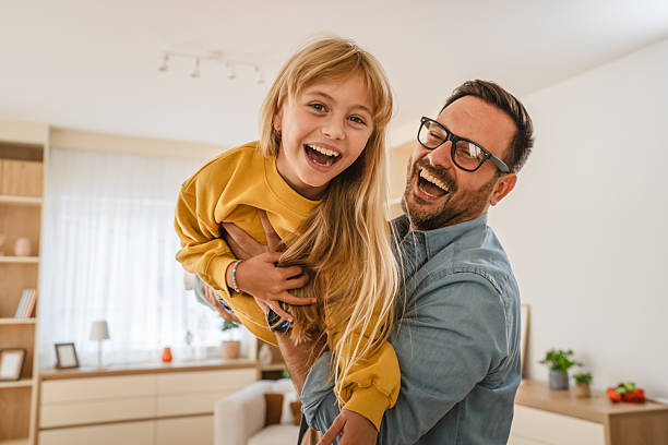 istock Father holding daughter, both laughing enjoying playtime at home 2239444296