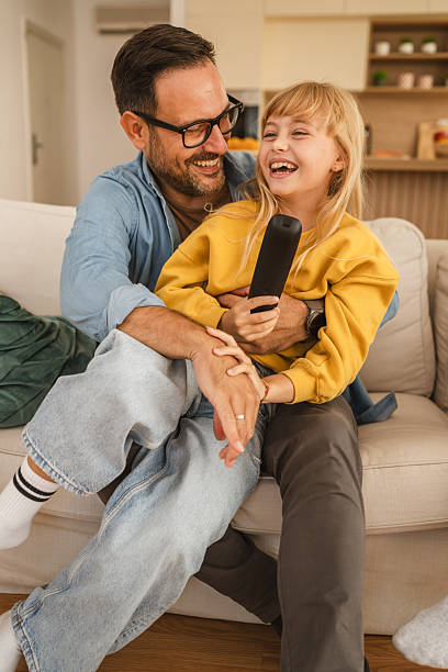istock Father and daughter laughing together watching television 2239444494