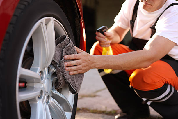 Man wiping car wheel with grey microfiber rag outdoors, closeup