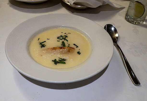 Mixed creamy pea soup with sliced fried bread, chive in white plate, cutlery, glasses with water, bowl with bread on restaurant table.