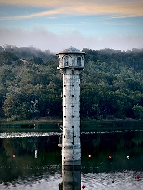 istock Old lighthouse on a reservoir surrounded by water and trees with hazy, cloudy sky in pastel 2239450413
