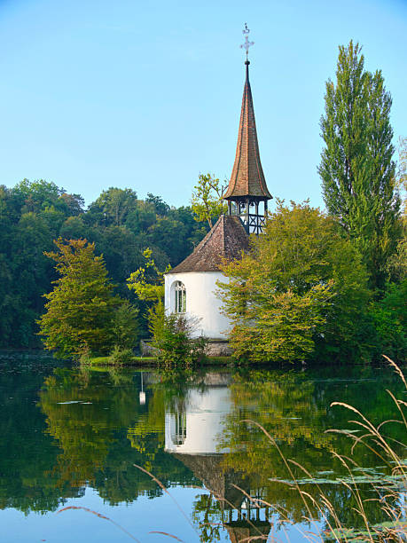 istock Charming lakeside chapel surrounded by trees on a clear day in a serene natural setting 2239454579