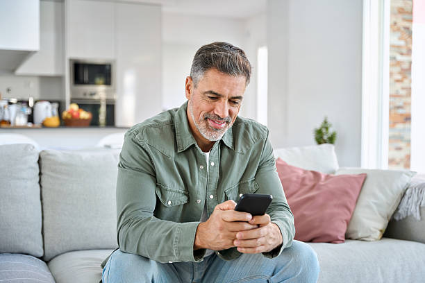 istock Middle aged old man using smartphone relaxing on couch at home. 2239455380