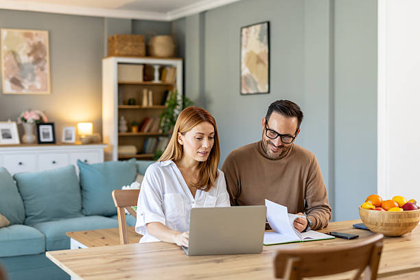 istock Couple at table using laptop and discussing financial papers 2239455750