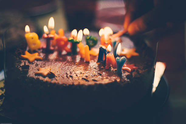 Birthday cake with a candle in the middle with young people around the table.