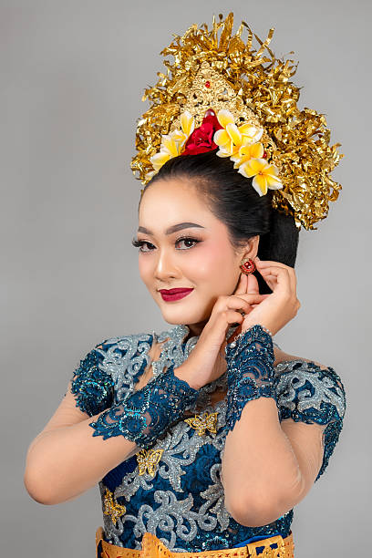 istock Confident Asian woman smiling gracefully with elegant expression, adjusting earring while wearing modern Balinese traditional costume and ornate gold headpiece adorned with flowers. 2239466003