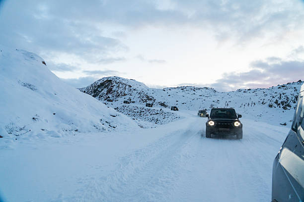 Murmansk, Russia - December 13, 2024: A line of dark Jetour T2 SUVs driving in a convoy on a snow-covered mountain road under a dramatic evening or twilight sky in the Arctic region