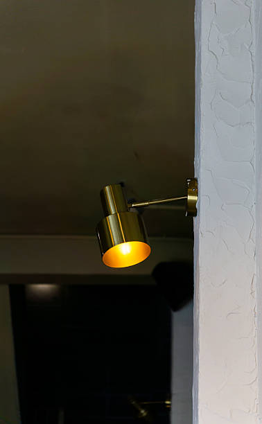 istock A brass wall-mounted spotlight with a warm yellow glow is attached to a textured white wall pillar 2239479044