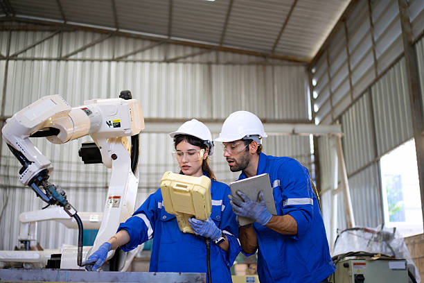 istock Blue collar workers at machine shop with welding robot arm. 2239480548