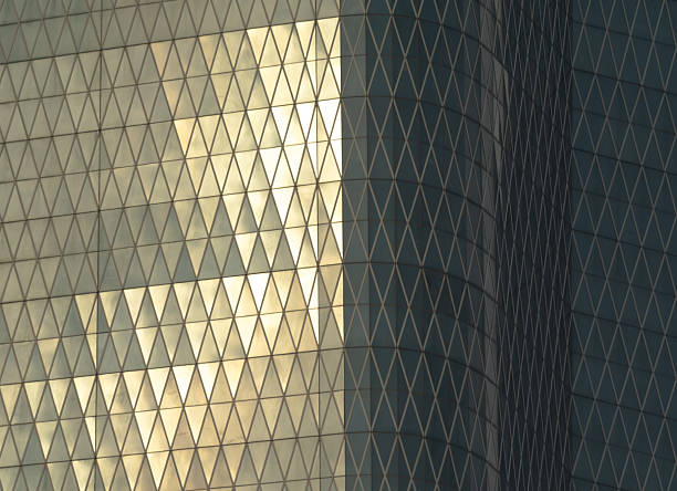 Stock image of a modern skyscraper exterior showcasing reflective glass windows illuminated by the warm sunlight in the afternoon. The architecture highlights geometric lines and mirror-like surfaces, creating a bright urban atmosphere. Perfect for illustrating concepts of business, finance, real estate, architecture, and modern city development.