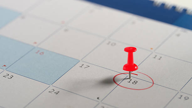 Red push pin marking date on calendar with circle around number 18. Appointment reminder and planning concept.