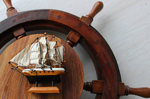 istock A wooden ship helm with a toy sailboat on it on a textured light oak board surface 2239492848