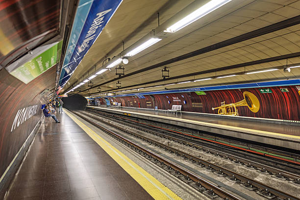 Anton Martin station, Madrid, Spain, Europe, September 10, 2025: Wide-angle view of the Anton Martin metro platform in Madrid, showcasing clean architectural lines, multiple tracks, and vibrant wall graphics including a large trumpet motif. The station features directional signage, yellow tactile paving for accessibility, and seated passengers waiting on benches.