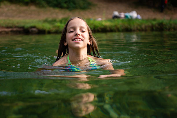 Happy girl smiling, swimming in a green river during summer, enjoying outdoor recreation and childhood