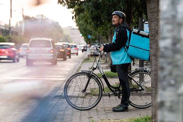 istock Delivery man with bicycle and backpack waiting in city traffic 2239497430