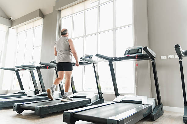 istock Man walking on a treadmill in a bright modern gym with large windows, multiple machines, and natural light, highlighting indoor cardio training and a healthy fitness routine. 2239498724