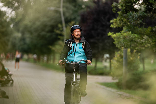 istock Delivery man riding bicycle in park wearing helmet and backpack 2239498974