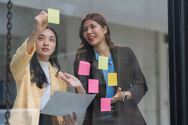 istock Businesswomen collaborating on ideas using sticky notes on glass wall 2239500443