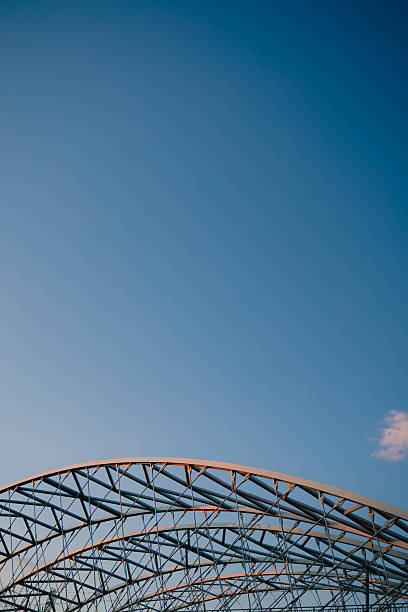 Vertical screen: curved metal beams creating robust and intricate framework rise against clear blue sky, highlighting elegance of industrial design and contemporary architecture. Modern architecture