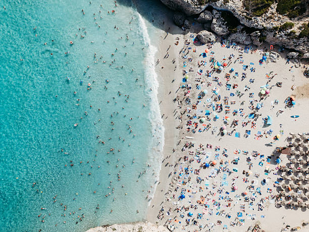 Crowded beach with people swimming in turquoise ocean water and relaxing under colorful umbrellas on a summer day
