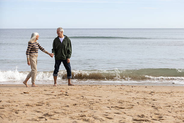 istock Senior Couple Walking Hand in Hand on the Beach 2239505534