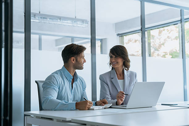 istock Mentor Latin hispanic woman and European intern man writing notes working using laptop computer in office. Two busy diverse colleagues, professional business people discussing project sitting at desk 2239510062