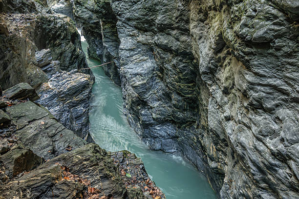 A narrow section of the Liechtensteinklamm gorge reveals steep, rugged cliffs and a winding turquoise river. The dramatic rock formations and fast-flowing water create a raw and powerful natural landscape deep within the Austrian Alps.