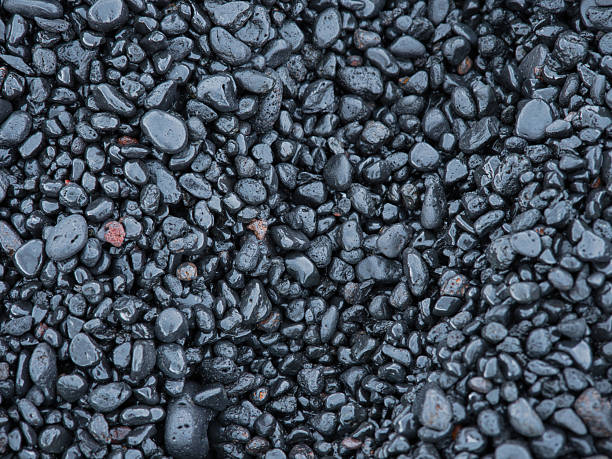 Stock photo showing close-up, elevated view of a pile of black stones on a sandy beach background.