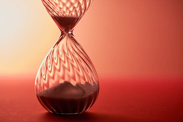 An hourglass measuring the passing time in a countdown to a deadline, on red background.
