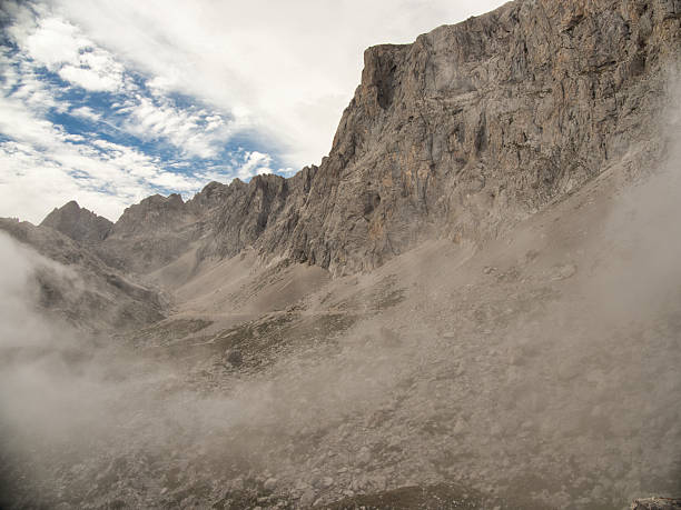 istock Towering sheer cliff face in misty gorge - Dramatic low-angle shot of a massive, vertical rock cliff with scree slopes disappearing into mist and fog in a high mountain gorge. 2239514264