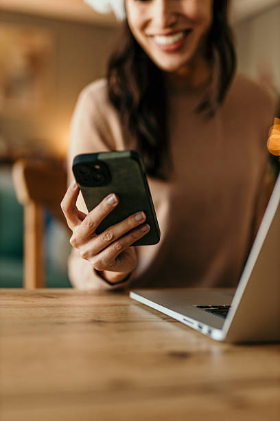Woman smiling using phone working on laptop remotely