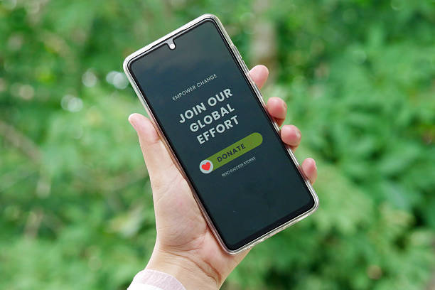 istock Hand holding smartphone displaying charity message build a brighter future donate button with green nature background sunlight 2239521581