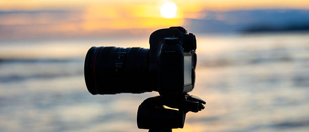 istock Camera with lens on tripod in golden hour by seaside. Camera in focus. 2239522626