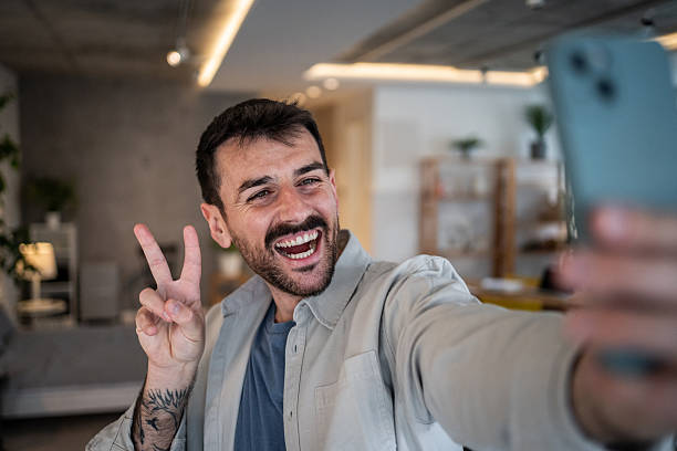 istock Man taking selfie, gesturing peace sign, laughing 2239522664