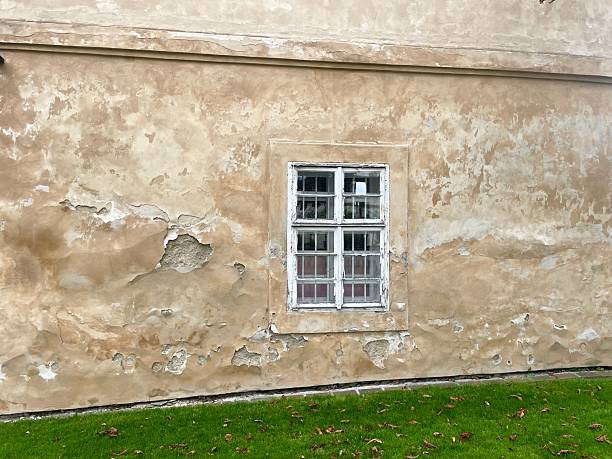 Old building. An uneven, lighthued wall that prominently displays a whiteframed window, contributing to its charm