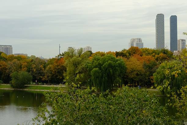 Novodevichey Park in autumn; autumn colors of green, yellow. brown;  lake in the park; behind sky scraper and city view; park in big city for resting