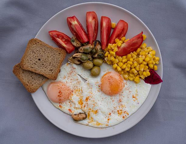 Close-up of a healthy breakfast plate with fried eggs, sweet corn, olives, mussels and fresh tomatoes served with whole grain toast. Balanced Mediterranean meal concept.