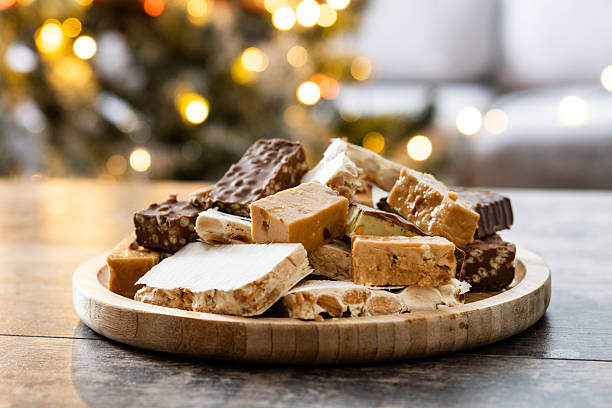 Assorted traditional Christmas nougat on wooden plate with candles in background