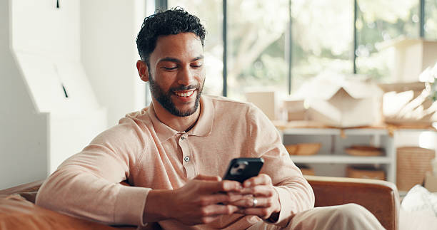 istock Smile, texting and man in home with mobile, doom scrolling and funny chat on app. Digital, meme and Asian male in living room with tech, virtual game or online communication in message update. 2239533217