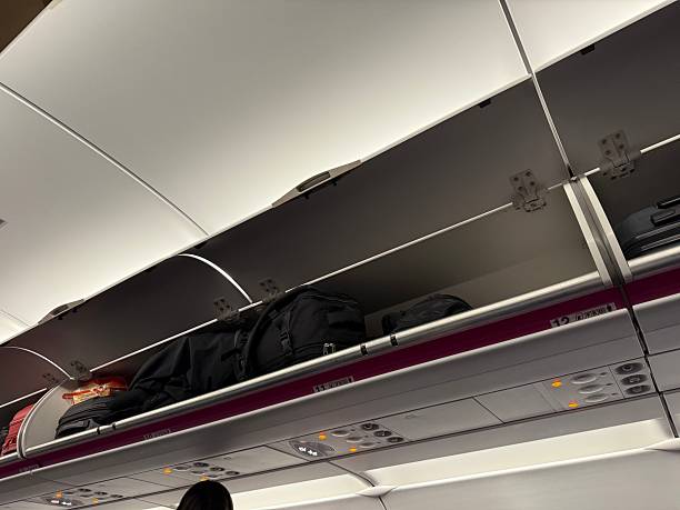 istock Open overhead luggage compartments with bags and personal items inside an airplane cabin, modern interior view 2239537385