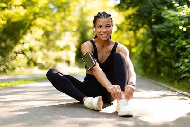 istock Smiling black woman sitting on jogging path outdoors, tying shoelaces before workout 2239544141