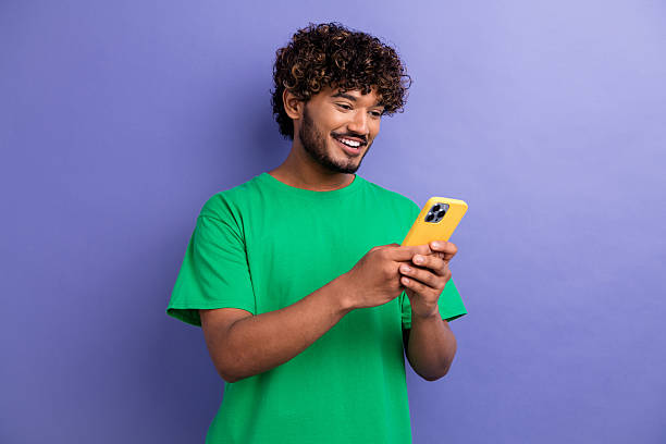 istock Happy young man in green t-shirt using smartphone with cheerful expression and enjoying casual lifestyle 2239546798