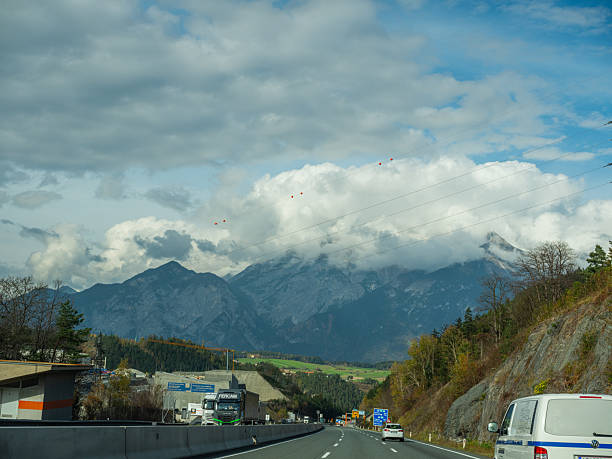 Austria, Europe.02.11.2022 Autobahn between Austria and Italy. road with fences along edges runs between low pictures que mountain covered with yellowing forests autumn. Cars are rushing along road