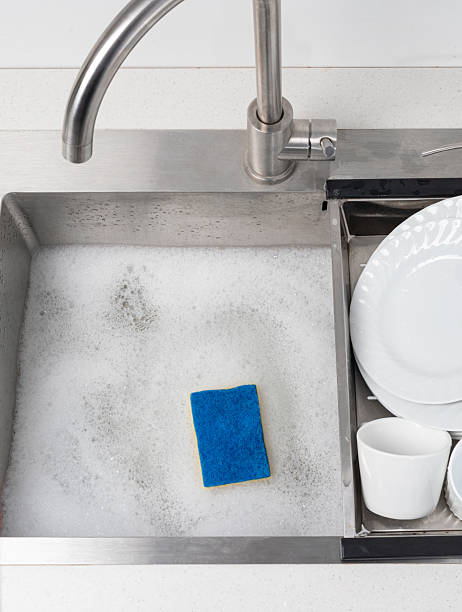 istock Blue sponge and soap suds in kitchen sink with dishes waiting to be washed 2239552264