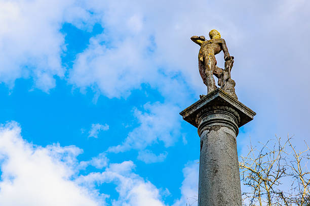 Ancient stone statue on tall column against blue sky and clouds. March 17, 2025, Konopiste Castle, Czech Republic.