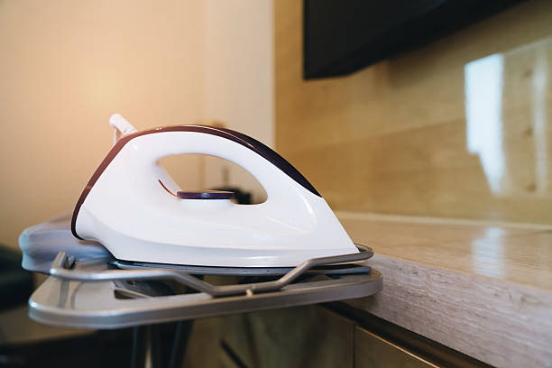 Modern iron appliance resting on a sleek ironing board in a well-lit home setting with warm sunlight in the background.