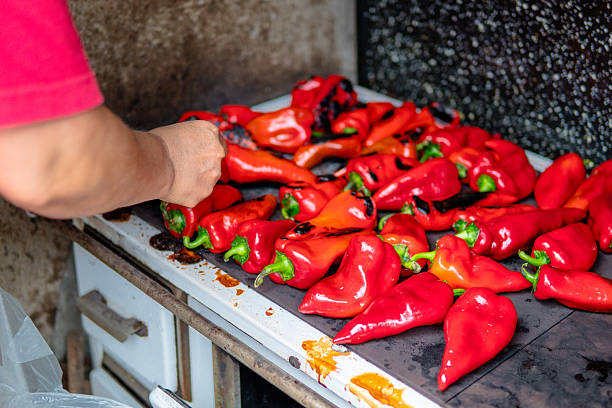Woman roasting red bell peppers. Close up of hands and papers.