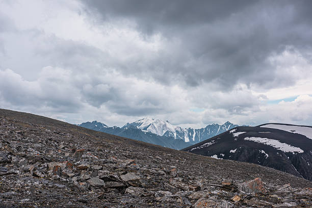 istock Dramatic alpine view from high stony pass to big snowy mountain top under gray cloudy sky. Large snow castle in gloomy rainy weather. Cold atmospheric landscape with sharp stones in wild mountains. 2239580286