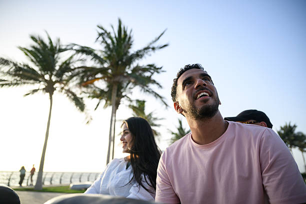 Cheerful young couple sharing a scenic ride along the Jeddah Corniche, surrounded by palm trees and coastal light as they enjoy a carefree outdoor moment near the waterfront.