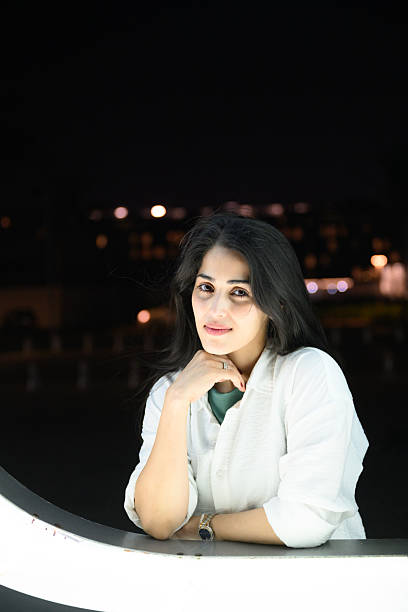istock Portrait of young woman looking at camera while leaning on an illuminated structure in night setting 2239582036